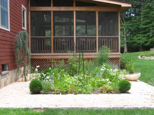 Herb and vegetable garden bed with gravel path by a screened porch