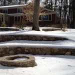 Natural stone fire pit nestled into curve in the wall.  Waiting for spring.
